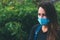 Close-up portrait of young woman in protective medical mask on her face, looking at camera outdoor.