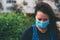 Close-up portrait of young woman in protective medical mask on her face, looking at camera outdoor.