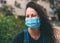 Close-up portrait of young woman in protective medical mask on her face, smiles and squints his eyes outdoor.