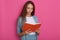 Close up portrait of young women reading something in notebook isolated over rosy background, looks concentrated, looking down,