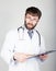 Close-up portret of a Doctor holding a map-case for note, stethoscope around his neck. He stares at the camera