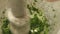 Close up pounding fresh herbs in a mortar with a pestle.