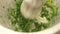 Close up pounding fresh herbs in a mortar with a pestle.