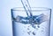 Close-up pouring water into glass on blue background