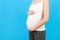 Close up of pregnant belly at blue background. Mother is wearing home clothing and holding her abdomen. Parenthood concept. Copy