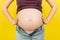 Close up of pregnant belly at colorful background with copy space. Future mother in opened jeans is embracing her naked baby bump