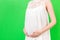 Close up of pregnant belly at green background. Mother is wearing white dress and holding her abdomen. Parenthood concept. Copy