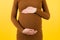 Close up of pregnant belly at yellow background. Mother is wearing brown dress and holding her abdomen. Parenthood concept. Copy