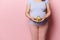 Close-up pregnant gravid woman holding a half of avocado fruit at the level of her big belly,  pink background