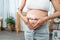 close up Pregnant teenage mother stands in the living room and makes a heart shape on her belly. show love