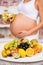 Close-up of a pregnant tummy with fresh fruit and plate of salad. Healthy pregnancy, diet and vitamins