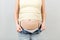 Close up of pregnant woman in elastic pregnancy bandage to make the pain go away at gray background with copy space. Orthopedic