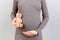 Close up of pregnant woman in gray dress holding teddy bear against her abdomen at gray background. Parenthood concept. Copy space