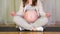 Close up of pregnant woman meditating sitting in yoga lotus position at home. Sports pregnant mother. Hands hug a