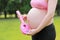 close-up of pregnant woman mother belly, hands hold children toy pink cartoon guitar in nature outdoor forest lawn meadow grass