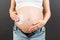 Close up of pregnant woman in opened jeans applying skin care cream on her belly to prevent stretch marks at colorful background