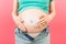 Close up of pregnant woman in opened jeans applying skin care cream on her belly to prevent stretch marks at colorful background