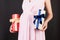 Close up of pregnant woman in pink dress holding two gift boxes at black background. Is it a boy or a girl Expecting twins.