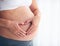 Close up of pregnant woman placing hands on belly in heart symbol