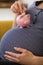 Close Up Of Pregnant Woman Putting Coin Into Piggybank Balanced on Her Stomach