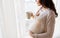 Close up of pregnant woman with tea cup at window