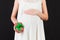 Close up of pregnant woman in white dress holding gift box at black background. Baby surprise concept. Happy pregnancy. Copy space