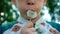 A close-up of a preschool boy holds a white dandelion in his face and inflates it towards the camera.