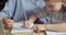 Close-up of preschool girl sitting with teacher educator at table at home or in kindergarten, learns to write draw on