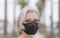 Close-up of pretty alone senior woman with medical mask due to coronavirus standing in a public park with high palm trees  - love
