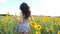 Close up of pretty girl running through sunflower field. Young woman in dress having fun jogging through meadow. Scenic