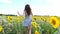 Close up of pretty girl running through sunflower field. Young woman in dress having fun jogging through meadow. Scenic