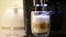 Close-up of the process of making latte coffee from modern coffee machine, poured in clear glass cup. Coffee machine is making fre