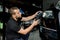 Close up of professional Caucasian male auto service worker, waxing and polishing headlight of black car with orbital