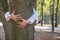 Close up of protective child hands embracing tree trunk in summer park. Care about nature concept