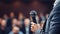 Close-up of a Public Speaker\\\'s Hand Holding a Microphone with a Blurred Audience at a Formal Event. Generative Ai