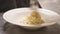 Close up of putting spaghetti carbonara with tongs into white serving bowl