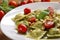 Close-up of Ravioli dish with fresh pesto sauce and cherry tomatoes, garnished with pine nuts and basil leaves