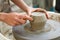 close up of raw ceramic running on the lathe or potter\'s wheel, with hands with tool refining fine details of vase