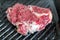 Close-up raw tasty fresh rib eye steak on grill cast iron pan. Organic beef meat seasoned with ground pepper coocked on barbeque