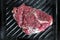 Close-up raw tasty fresh rib eye steak on grill cast iron pan. Organic beef meat seasoned with ground pepper coocked on barbeque