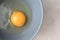 Close-up raw uncooked egg in gray bowl with copy space, top view. Yellow egg yolk and liquid egg whites. Ingredient for baking