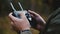 Close-up rear view male hands controlling drone aircraft using modern remote control with smartphone in autumn forest.