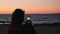 Close up rear view of young woman making photos and videos of beautiful sea sunset. Attractive female takes pictures standing on s