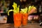 Close up of red bloody mary cocktails on bar top with green fresh celery leaves and bartender at night