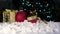 Close up of Red bobbles and parcel on white snow with Chritmas tree lights flickering in background. shallow depth of