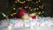 Close up of Red bobbles and parcel on white snow with Chritmas tree lights flickering in background. shallow depth of