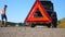 Close up of red emergency stop sign standing on road. Worried and angry driver walking near his broken car talking on