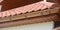 A close-up on red metal tile rooftop with wood soffit, house eaves, rafters and installed rain gutter