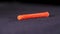 Close up of red plastic building dowel lying on the dark grey surface. Stock footage. Orange dowel, details of the