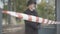 Close-up of red and white tape barrier with blurred man in coat and hat standing at the background. Unrecognizable